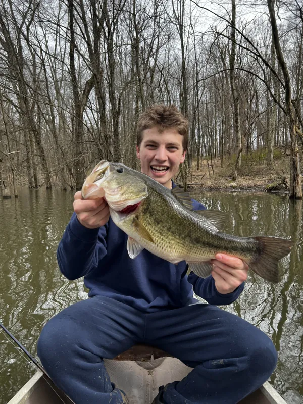 A laughing angler in a canoe among flooded trees holds up a largemouth bass